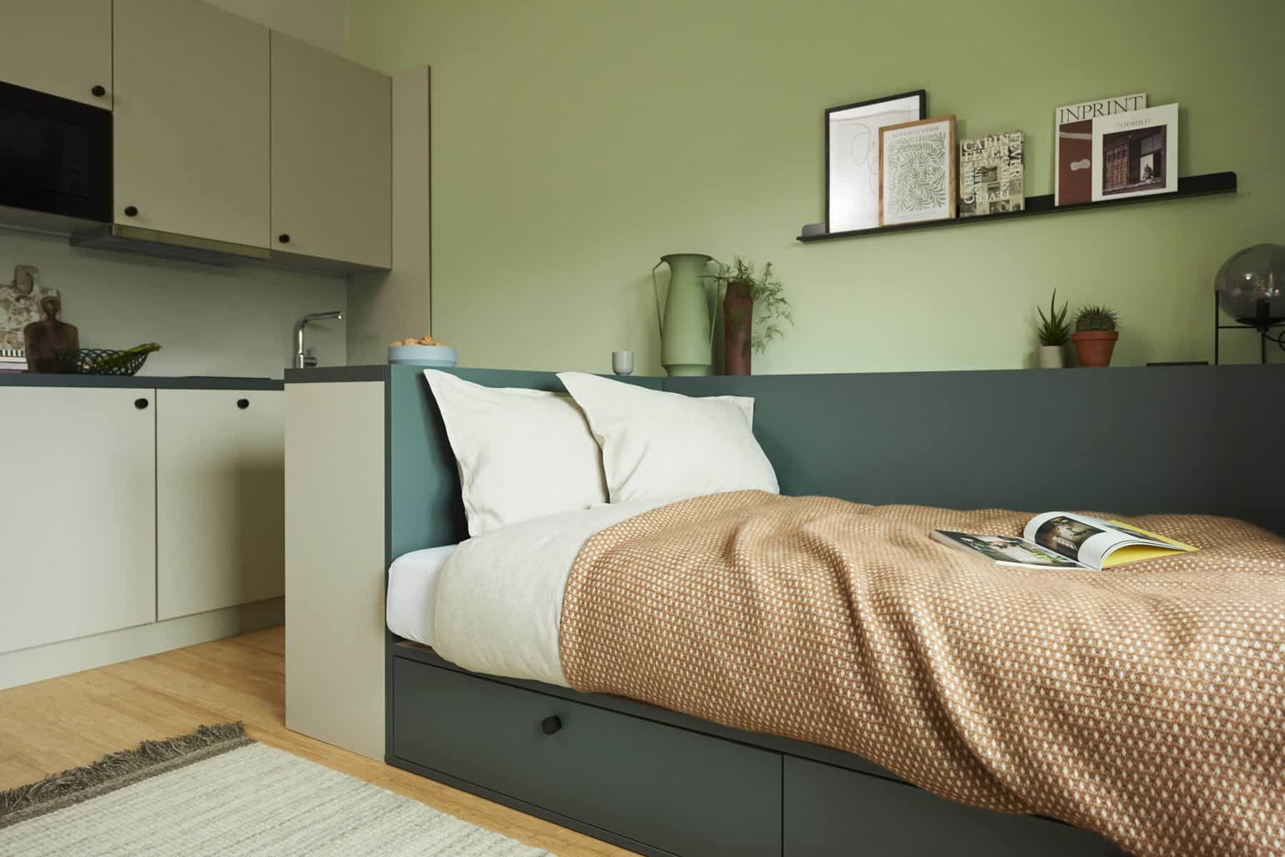 Studio vom Typ B im The Bloom Homes mit Bett vor salbeigrüner Wand und Küchenzeile
