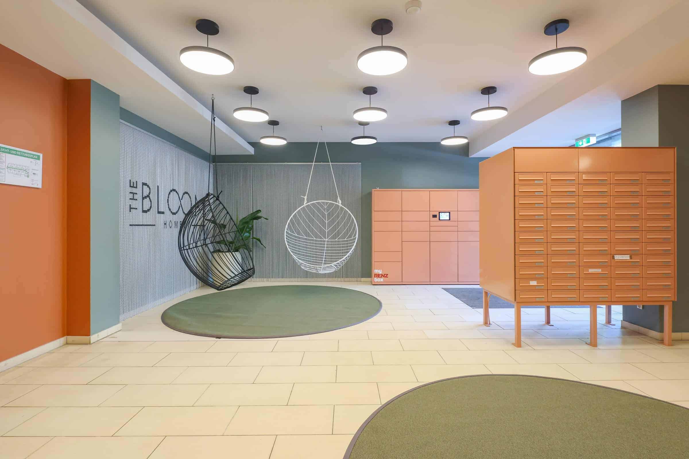 Eingangshalle im The Bloom Homes mit Hängesesseln, Paketstation und Schriftzug des Hauses