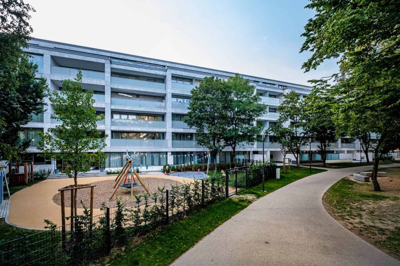 Das Roomments in Stuttgart-Mitte von außen: heller Riegel mit umlaufenden Balkonen, davor Bäume und Rasen
