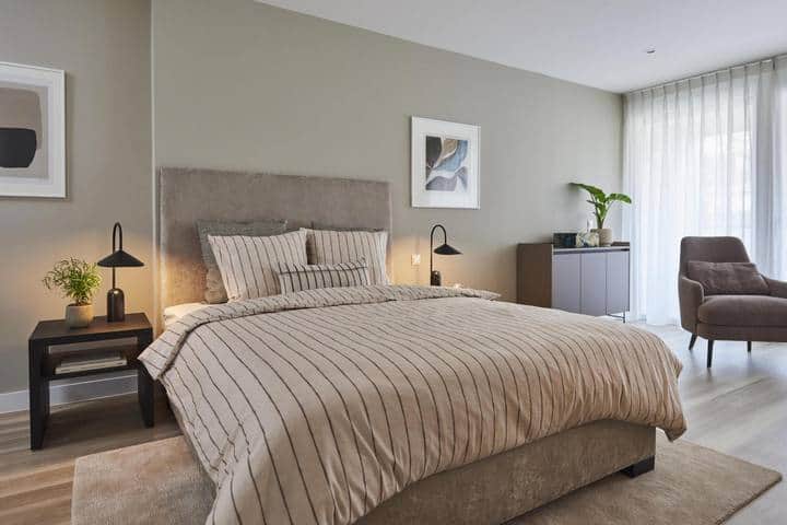 Schlafbereich im Roomments Smart mit Doppelbett, Sessel und bodentiefem Fenster